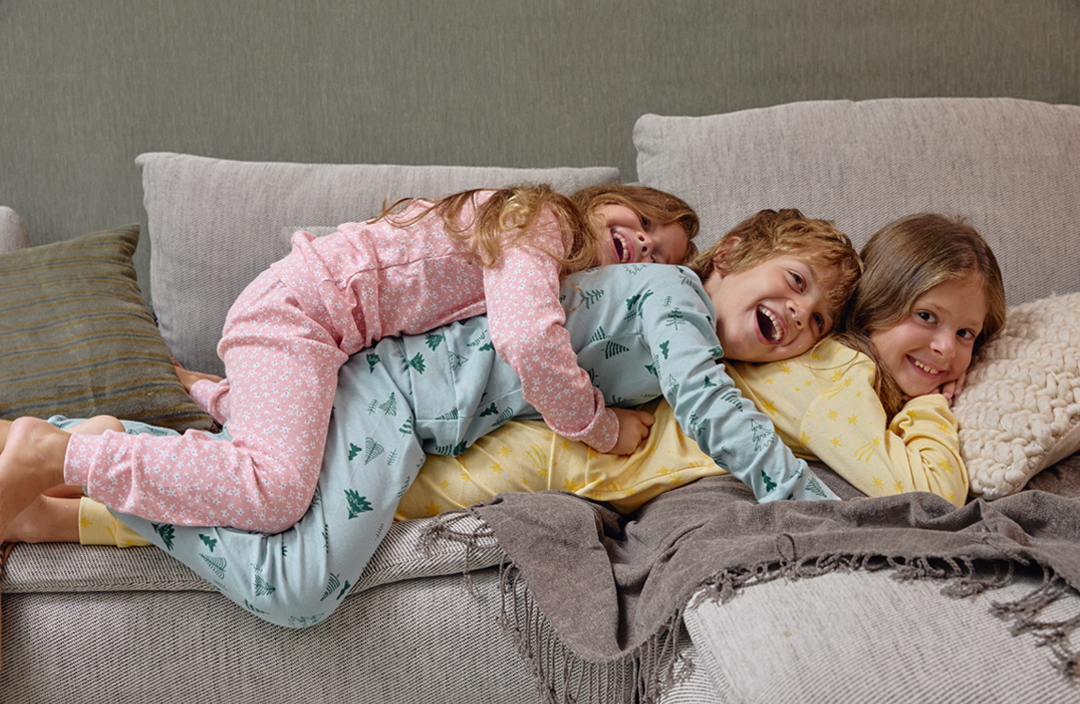Dječak i dve djevojčice leže na krevetu u šarenim pidžamama