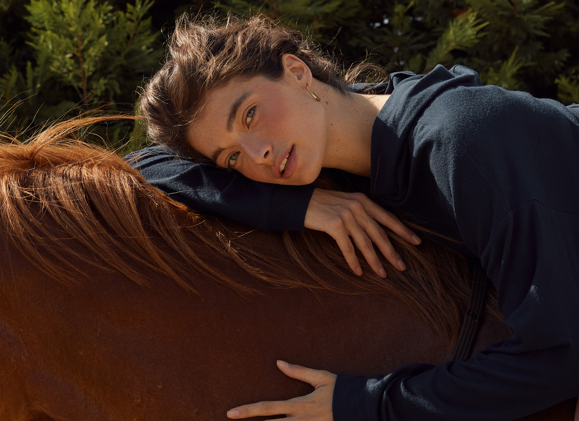 Djevojka u teget duksu sa kapuljačom sedi na konju
