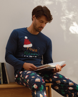 Muškarac u novogodišnjoj  pidžami na dug rukav drži knjigu 